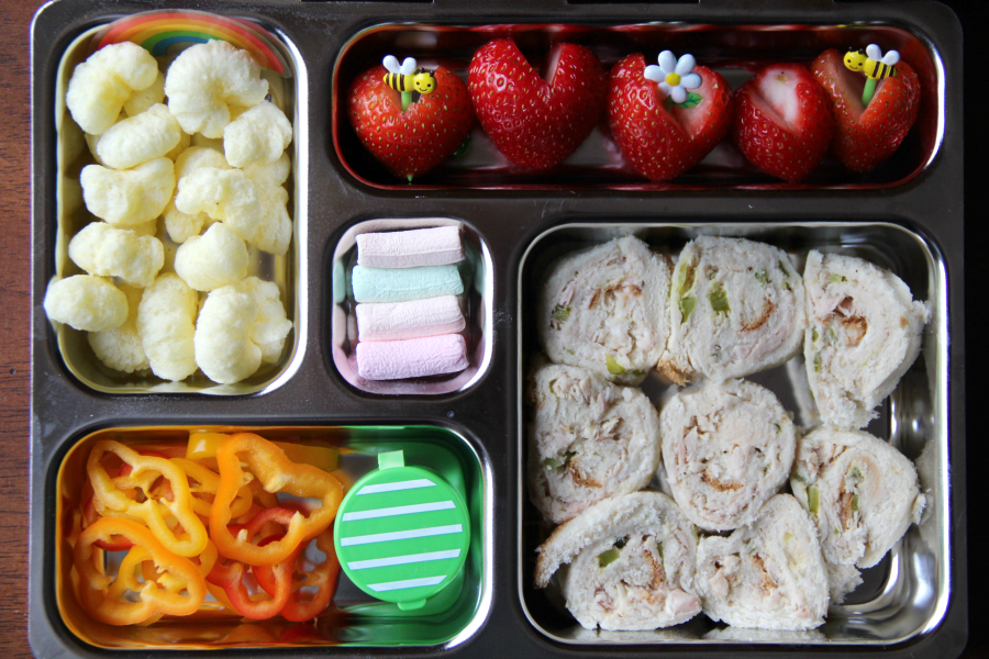  Top down image of Planetbox lunch packed with tuna salad sandwich rollups, Pirate Booty, strawberries, sweet peppers with dip and mini marshmallows for dessert.