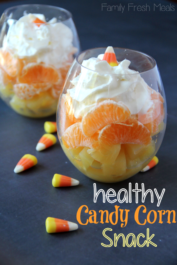 2 Healthy Halloween Snack Candy Corn Fruit Cocktail sitting on a black table with candy corn candies scattered around glasses