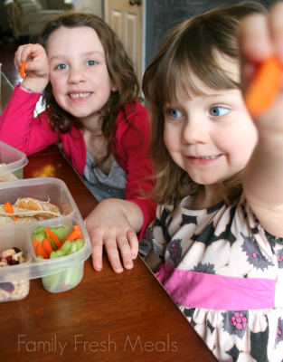 2 children sitting at a table with with lunchboxes