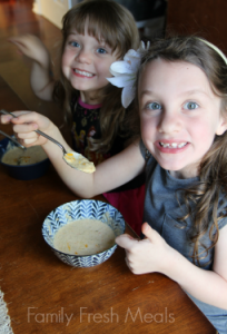 2 children sitting at a table eating soup