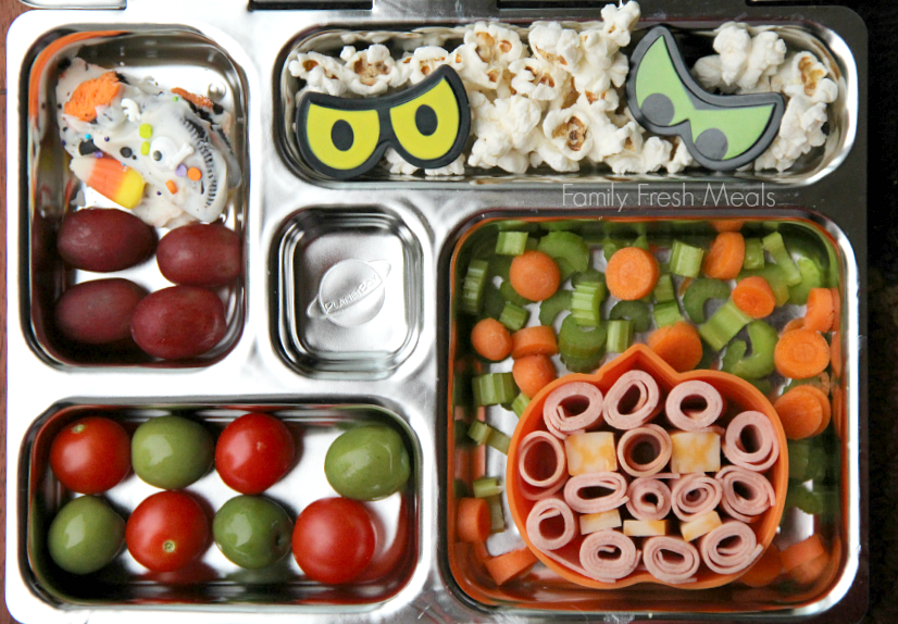 Planetbox lunchbox  packed with carrot, celery, rolled up lunch meat and cheese, cherry tomatoes and olives, Halloween Bark , grapes and some popcorn.