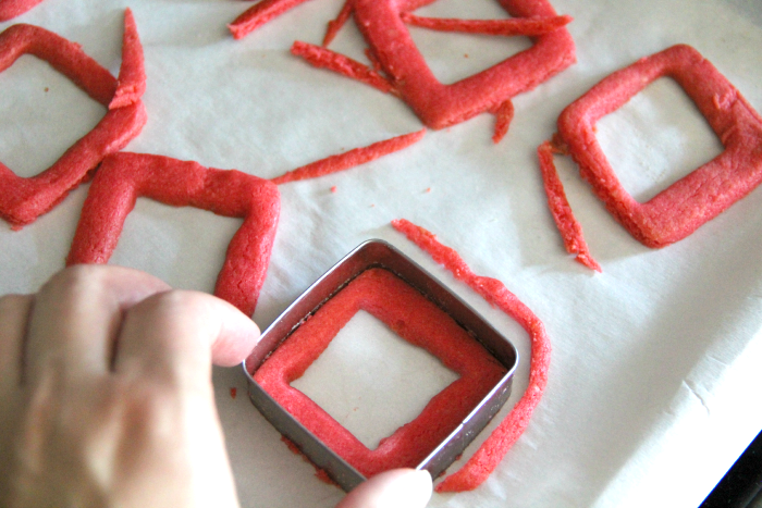 cutting red dough with square cookie cuter