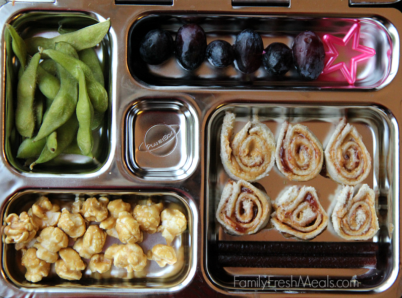 Planetbox lunch packed with grapes, edamame, caramel corn, almond butter and jelly sushi and fruit leather. 