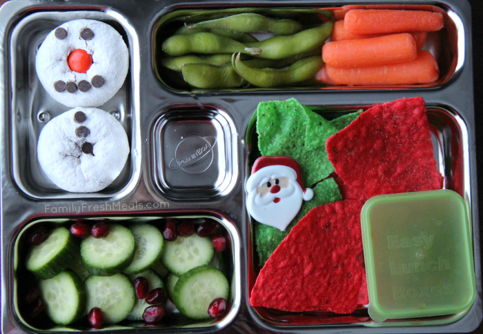 Lunchbox packed with steamed edamame, carrots, tortilla chips and salsa, cucumbers with pomegranate seeds and a mini donut snowman for dessert. 