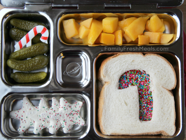 top down image of lunch box packed with mango, dill pickles, a fairy bread sandwich, and a couple star shaped cookies for dessert. 