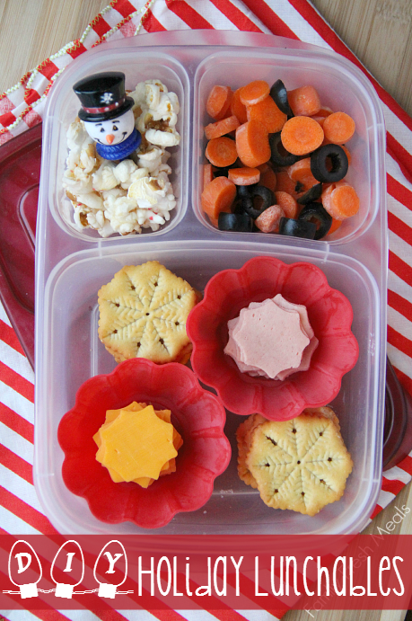 Lunchbox packed with snowflake crackers, deli meat and cheese cut with a snowflake cookie cutter.  In the smaller compartments are some carrot coins, olives and popcorn.