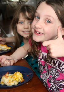 two children sitting at a table eating breakfast casserole