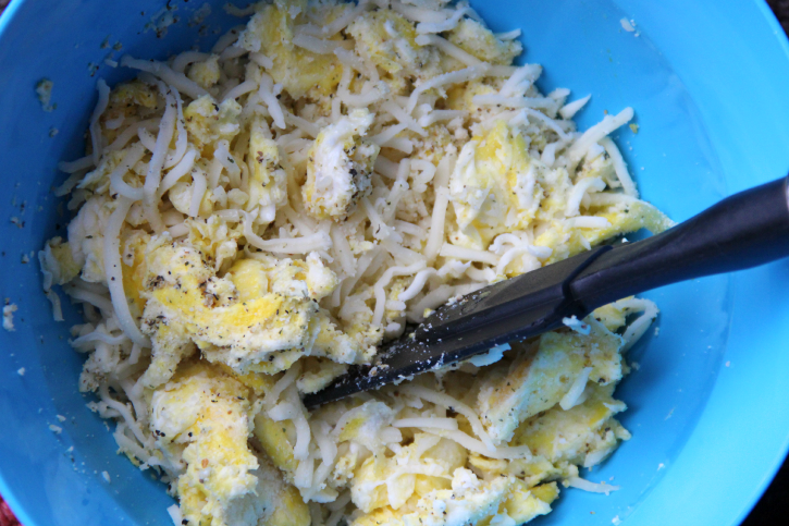 Mixing together scrambled eggs, Parmesan cheese and all purpose seasoning in a blue bowl