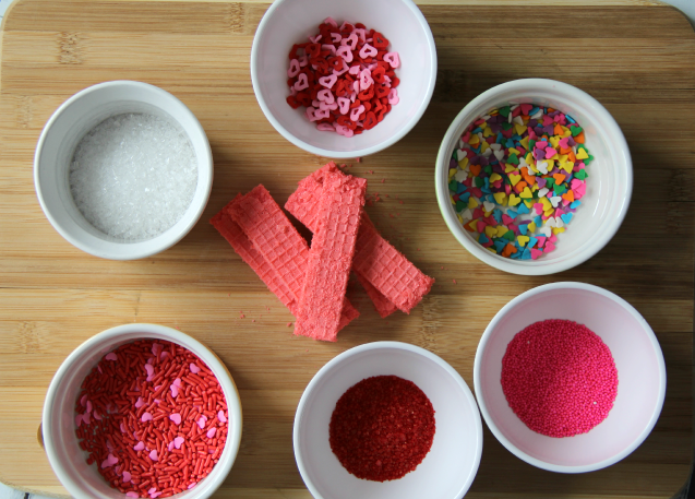 pink wafer cookies and a variety of sprinkles in small white bowls