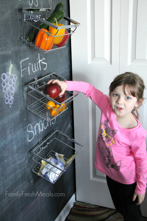 child taking a piece of fruit from the hanging baskets