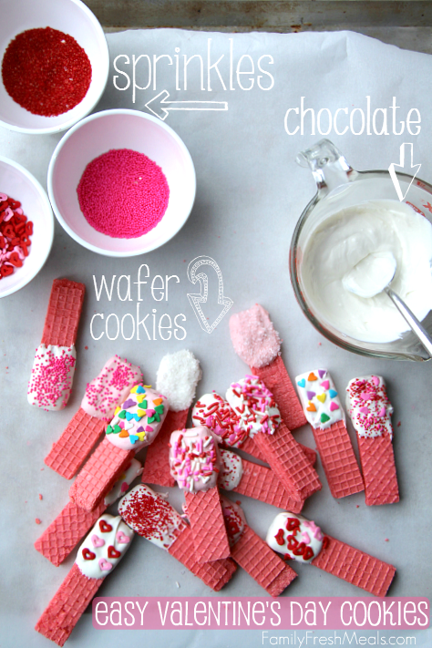 Valentine's Day Cookies laid out on parchment paper with sprinkles, and melted chocolate