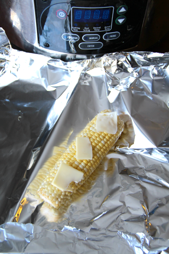 Corn on the cob on a piece of foil with 3 tabs of butter on top