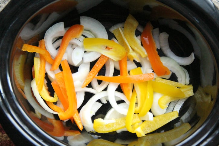 Bell peppers and onions in bottom of a slow cooker