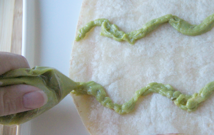 squeezing guacamole out of ziplock back, making wavy lines on quesadilla 