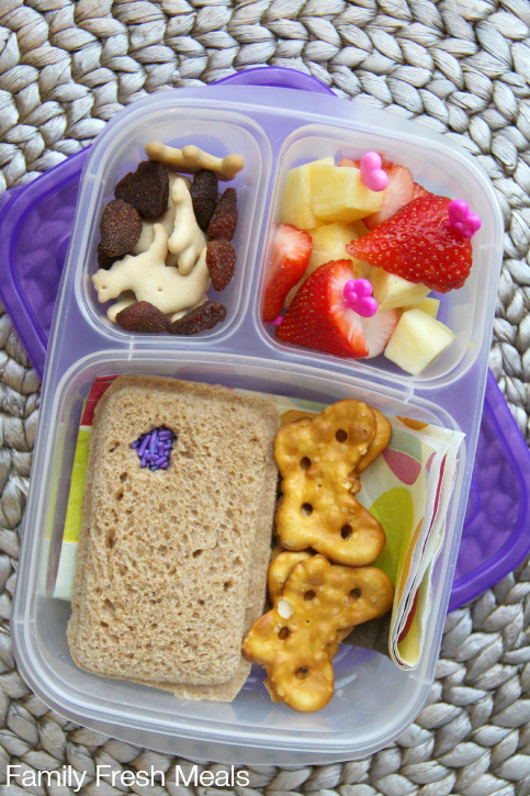 Pocket sandwich, pretzels, fresh fruit, animal crackers and some dried strawberries packed in a lunchbox