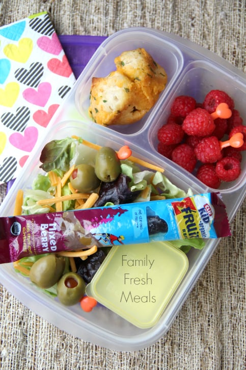 salad packed in a lunch box container with raspberries and a roll