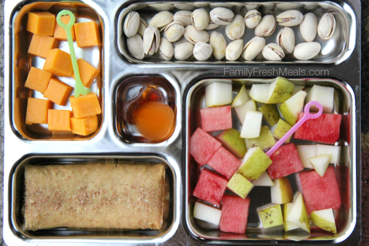 Watermelon, pears, pistachios, cheese cubes, a breakfast bar and some fruit snacks - packed in a metal lunchbox 