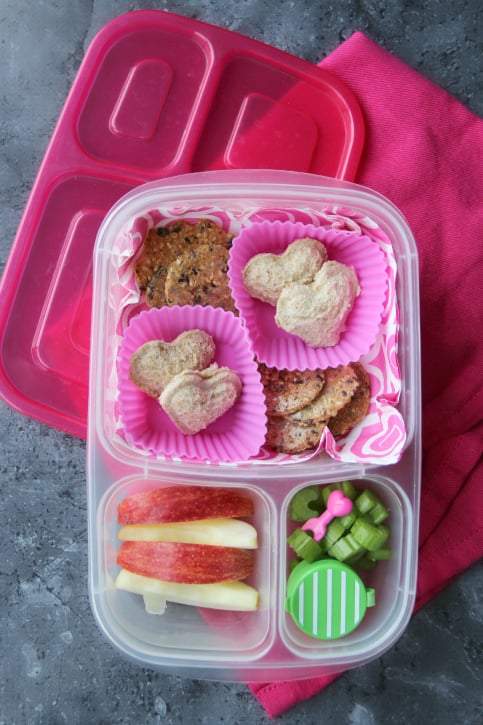 Mini heart pocket sandwiches packed in a lunchbox with apples, celery and crackers