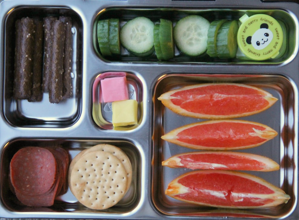 mini cucumbers with a container of dip, pretzel rods, some orange slices, crackers, turkey pepperoni and a couple pieces of candy for dessert - packed in a metal lunchbox