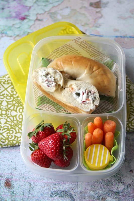 Stuffed Bagel Sandwich packed in a lunch box with strawberries and carrots