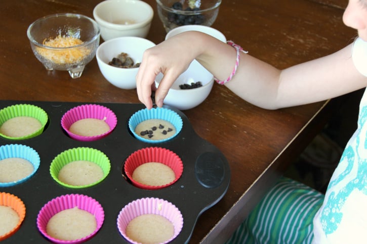 Child adding pancake mix- in ingredients to pancake muffins