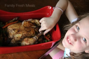 child sitting next to the roasted chicken in a serving platter