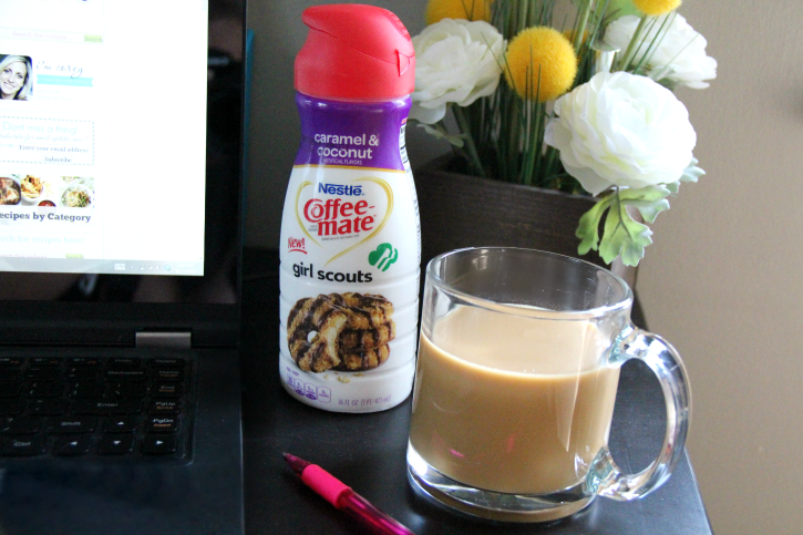 A cup of coffee and creamer next to a lap top computer