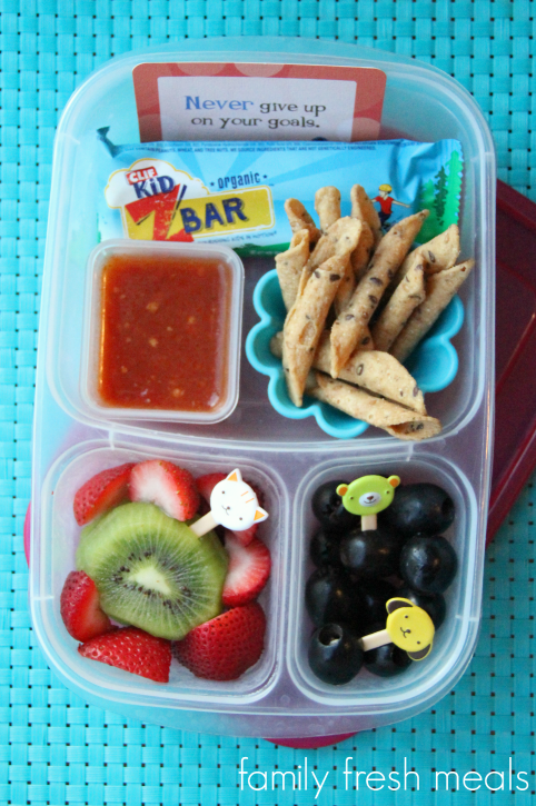 Chips, salsa, Cliff Bar, black olives, and some fresh fruit packed in a lunchbox