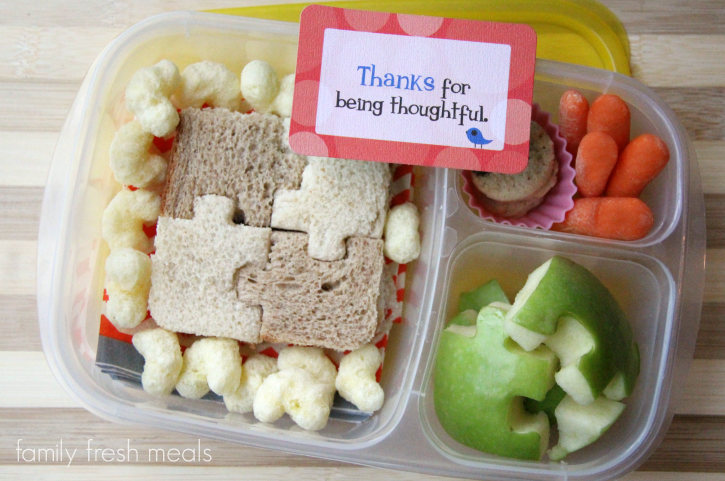 puzzle shaped sandwich, cheddar puffs, apples, carrots and some mini cookies packed in a lunch box