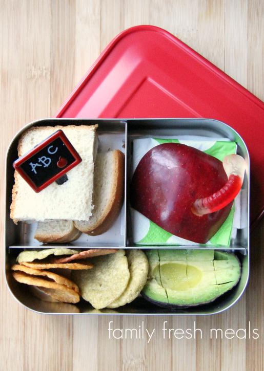 half sandwich ,avocado, chips, apple and a gummy worm packed in a lunchbox