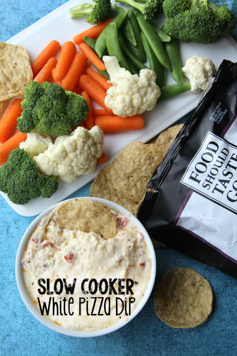 Slow Cooker Cheesy White Pizza Dip in a small white bowl with vegetables and chips