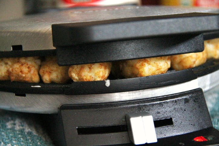 Tater Tots being pressed with a waffle iron