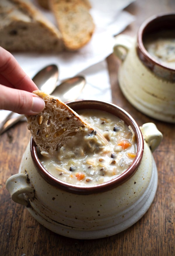 Chicken wild rice soup in a small bowl, with a piece of bread dipping into it