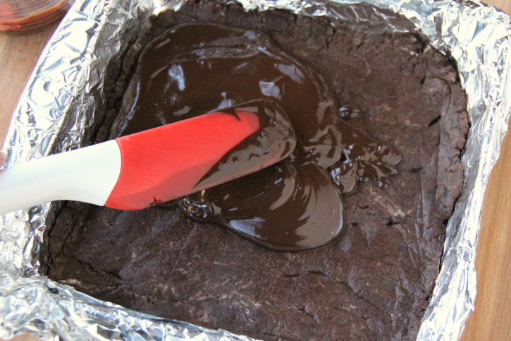 spatula spreading chocolate mixture over fudge 