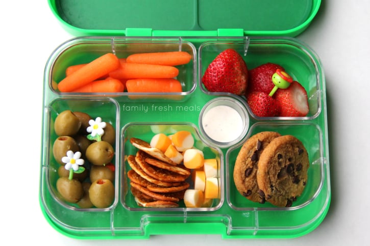 Carrots and dip, olives, pretzel crackers, cheese, strawberries and some cookies packed in a lunch box