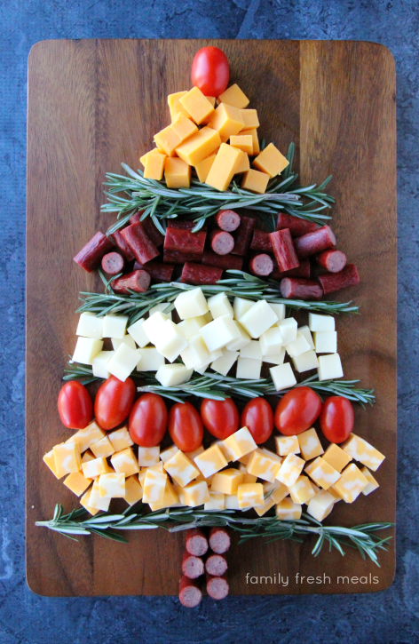 Christmas tree shaped appetizer made of cubed cheese, rosemary, sausage bites and cherry tomatoes