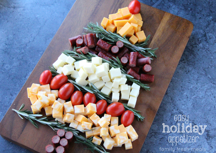 Christmas tree shaped appetizer made of cubed cheese, rosemary, sausage bites and cherry tomatoes