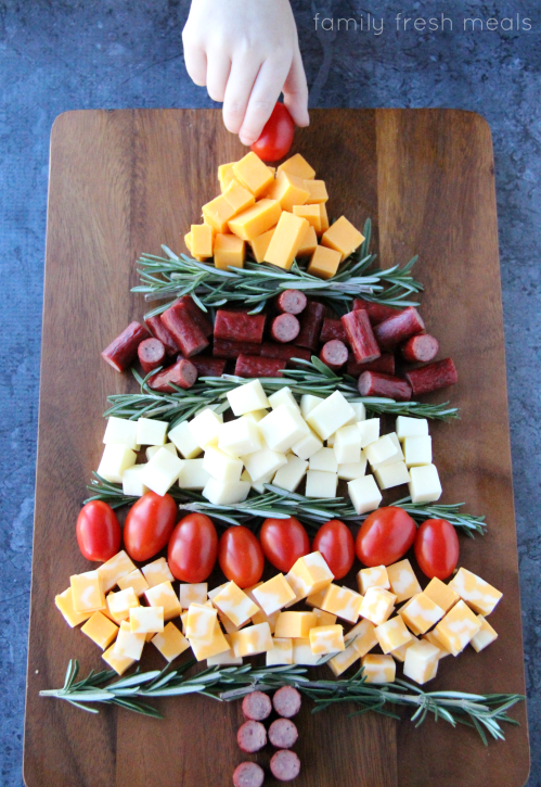 a hand placing a cherry tomato at the top of the appetizer Christmas tree