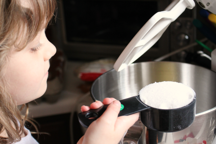 Child holding a measuring cup of flour over mixing bowl