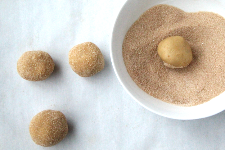 cookie dough being rolled in cinnamon sugar mixture