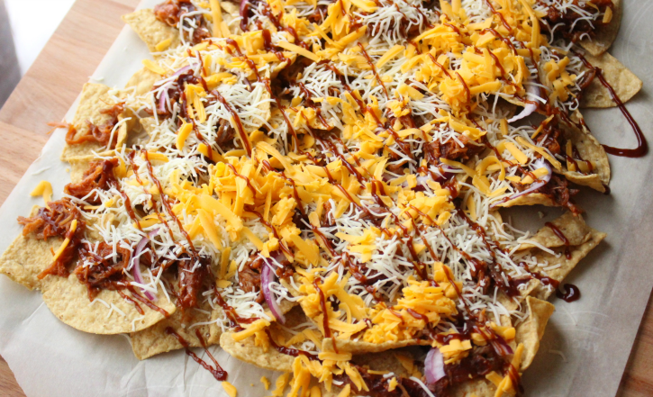 shredded cheese and bbq sauce being added to nachos