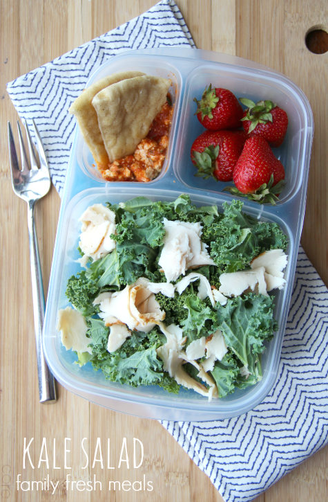 Pizza dip, pita chips, strawberries and a kale salad packed in a plastic lunch box