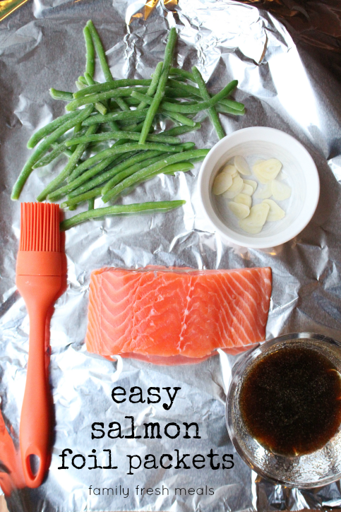 salmon, green beans, garlic slices and a brown sauce in a bowl - sitting on aluminum foil