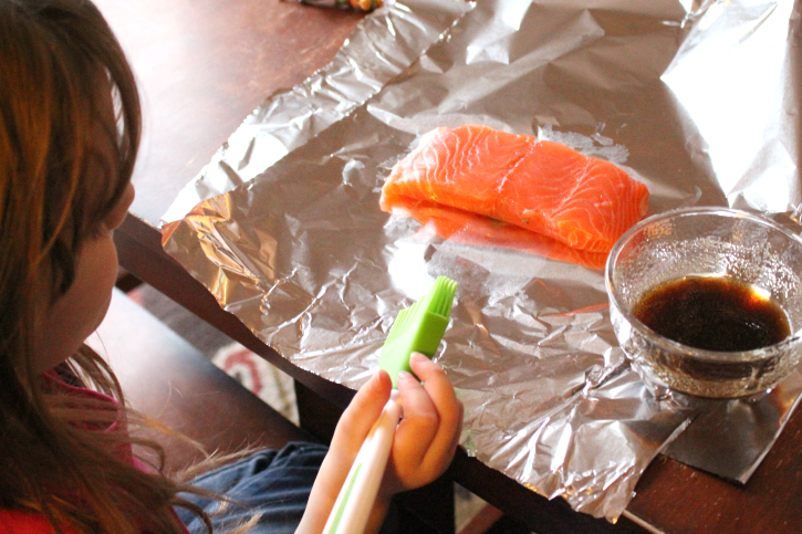 child sitting in front of a piece of salmon that is sitting on foil