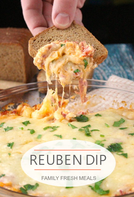 A hand dipping a small piece of bread into Reuben Dip 