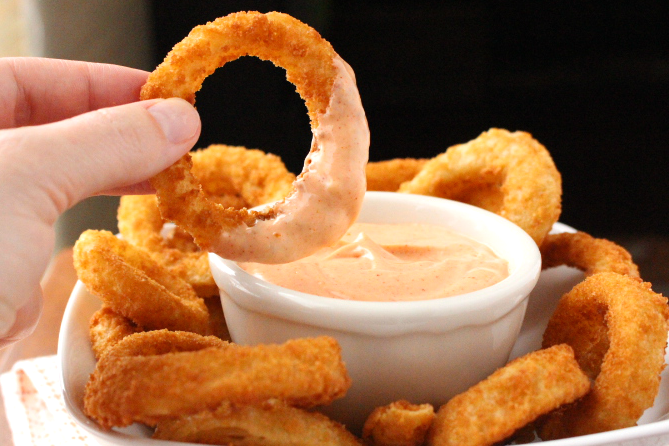 Onion ring being dipped into Copycat Outback Blooming Sauce