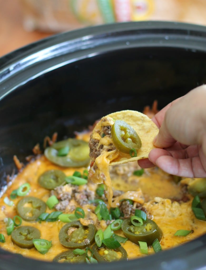 bean dip in a slow cooker with a tortilla chips scooping some up