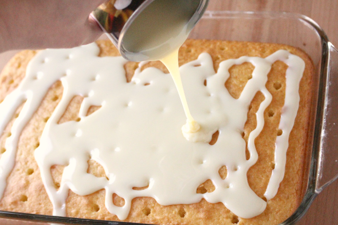 pouring condensed milk over cake with holes
