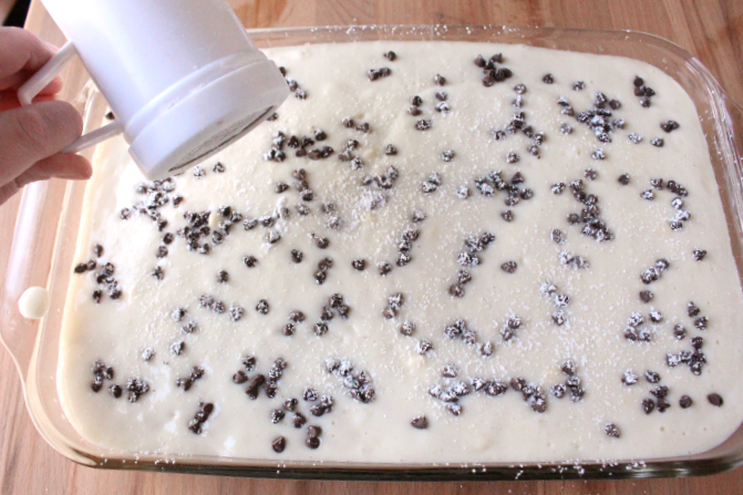 shaking powdered sugar over cake Cannoli Poke Cake 