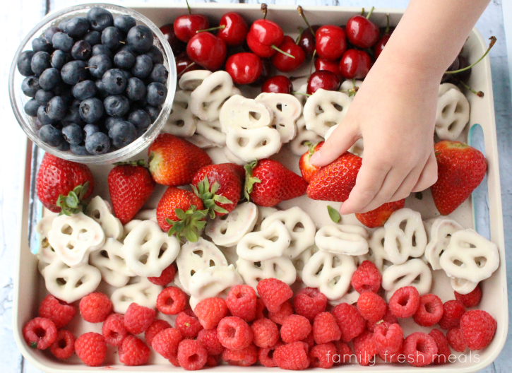 Easy Flag Fruit Dessert on a serving platter and a hand picking up a strawberry from the dessert